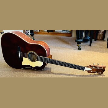 Akustická kytara s tmavě hnědým, lakovaným povrchem těla a viditnou masivní strukturou dřeva na bocích. Nástroj má světlý pickguard a tmavý hmatník s…