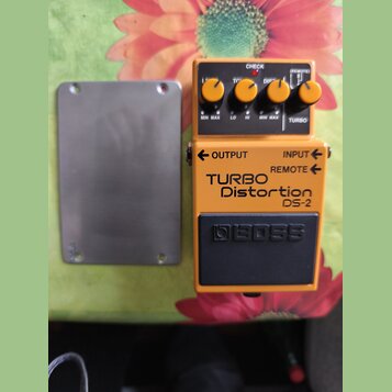 Kytarový efekt pedál oranžové barvy s černým spínacím tlačítkem. Na přední straně je nápis TURBO Distortion DS-2 a logo BOSS. V horní části jsou čtyř…
