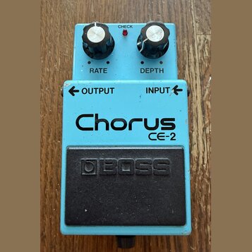 Modrý efekt pedál s nápisy Chorus a CE-2. Na horní části jsou dva černé ovratovky s popisky RATE a DEPTH, červená kontrolka CHECK a vstupy OUTPUT a I…