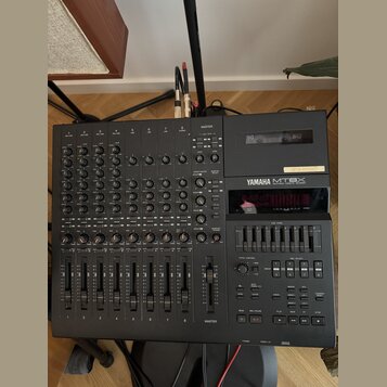 Černý multitrackový kazetový nahrávač s integrovaným mixážním pultem. Na přední straně je nápis YAMAHA MT8X MULTITRACK CASSETTE RECORDER. Zařízení ob…