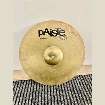 Kruhové mosazný činel s viditelným povrchovým opotřebením a skvrnami. Na povrchu je černý nápis pAiste, pod ním text 16" CRASH a vedle loga označení…
