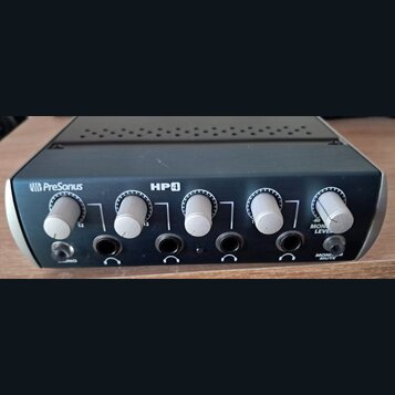 Černý distribuční zesilovač sluchátek s pět vệmi stříbrnými ovládacími knoflíky. Na předním panelu jsou nápisy PreSonus a HP4, u posledního knoflíku…