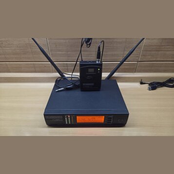 Černý bezdrátový přijímač s dvěma anténami a nápisem LD SYSTEMS WS1000/QR. Na přední straně je oranžový displej s hodnotou 826.300 MHz a řada kontrol…