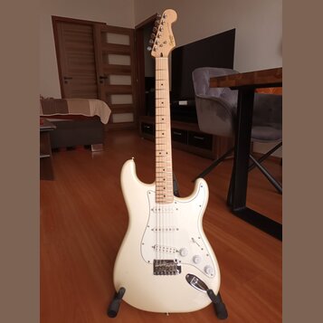 Bílá elektrická kytara typu Stratocaster s bílým pickguardem a javorovým hnedým hmatníkem. Na hlavě nástroje je viditelné logo Squier. Kytara má tři…