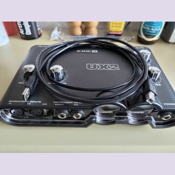 Černý zvukový interface Line 6 UX2 s kovovými ovratky. Na přední straně jsou viditelné nápisy MICROPHONE INPUTS 1/L, 2/R, +48V a INSTRUMENT INPUT NOR…