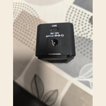 Černý plastový adaptér s dvěma konektory. Na horním je nápis USB, pod ním se nachází port USB-C. Spodní konektor je kulatý a nad ním je text DC 12V 3…