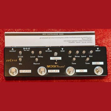 Černý efektový pedál s nápisem MOSKYAudio®. Zařízení obsahuje čtyři stoupací spínače označené jako REVERB, DELAY, OD a DS. Na horní části jsou umístě…