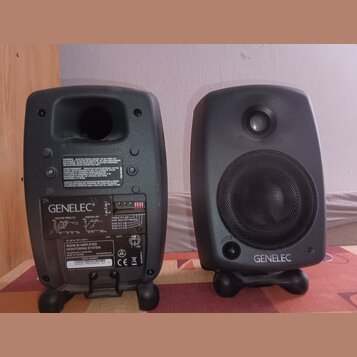 Dva šedé studiové monitory značky GENELEC. Na zadní straně levého reproduktoru je vidět nápis „GENELEC“, modelové označení „8020B BI-AMPLIFIED MONITO…