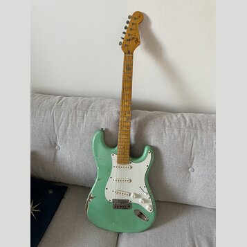 Světle zelená elektrická kytara s bílým pickguardem a javorovým hmatníkem. Na hlavě je viditelné logo Fender. Lak na těle vykazuje výrazné opotřebení…