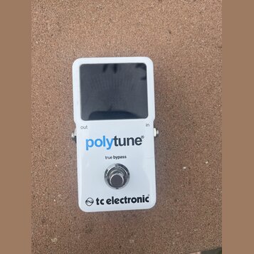 Bílý kytarový ladič s černým displejem. Na přední straně je modrý nápis polytune®, pod ním text true bypass a ve spodní části logo tc electronic®. Na…