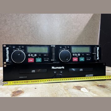 Dvě černé jednotky Numark CDN22 Professional CD Player. Horní zařízení má dvě ovládací jog-kola, displeje a tlačítka CUE a PLAY/PAUSE. Spodní zařízen…