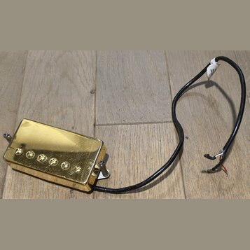 Zlatý humbucker s kovovým krytem a šesti viditelnými šrouby v polosičce. K snímači vede černý kabel s odhalenými koncovými vodiči a bílým papírovým š…