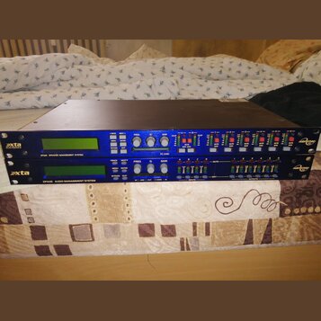 Dva modré rackové procesory značky xta electronics naskládané na sebe. Horní jednotka nese nápis DP226 SPEAKER MANAGEMENT SYSTEM a spodní DP446 AUDIO…