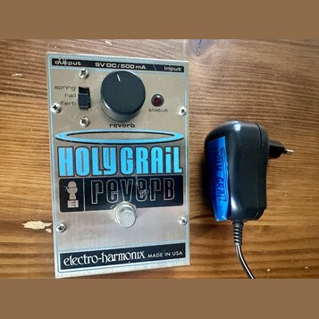 Kytarový efekt s kovovým stříbrným povrchem a nápisy HOLY GRAIL reverb. Na zařízení je černý ovládací knoflík s popiskem reverb, přepínač s nápisy sp…