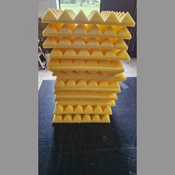 Stoh žlutých akustických absorbů z pěny s pyramidovým povrchem. Panely jsou naskládány na sebe na tmavém podkladu. Na fotografiích nejsou viditelné ž…