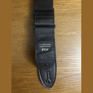 Černý popruh z kombinace textilu a kůže. Na koženém části je bílým nápisem vyrazeno Genuine Leather Made in Canada a pod tím kód F7GP. Povrch kůže vy…