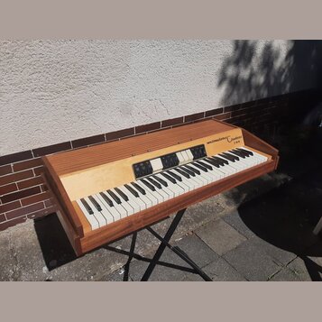 Elektronický klavír v dřevěném korpusu hnědé barvy. Na pravé straně horní desky je nápis weinmeister Clavisei a pod ním označení 2000. Nástroj má bíl…
