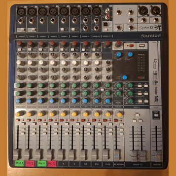 Míčovací pult značky Soundcraft, model Signature 12. Zařízení má šedé tělo s modrým horním panelem a obsahuje řadu knoflíků, posuvníků a vstupních ko…