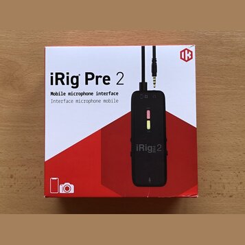 Fotografie znázorňuje krabici s produktem iRig Pre 2. Na bílo-červeném obalu je uveden název „iRig Pre 2“ a popis „Mobile microphone interface / Inte…
