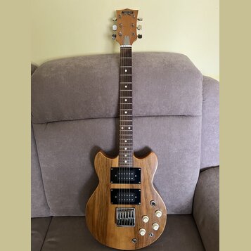 Elektrická kytara s přírodním dřevěným povrchem a hnědým hmatníkem. Na hlavě je nápis "Superstar". Nástroj má dva černých humbuckery, čtyři bílé ovlá…