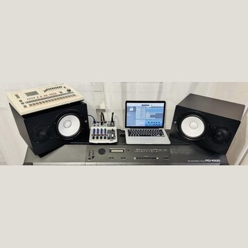 Sestava hudebního vybavení na šedém podkladu. V popředí je digitální piano s nápisem ROLAND DIGITAL PIANO RD-1000. Nad ním jsou dva černé studiové mo…