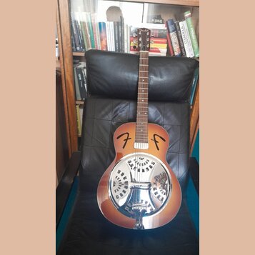Akustická kytara typu resonator s hnědým gradientním lakem a chromovaným kovovým rezonátorem. Na hlavě hředu je bílý nápis Fender a na těle jsou dvě…