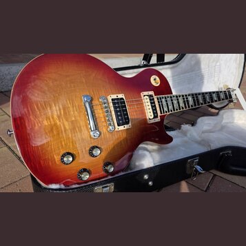 Elektrická kytara s tvarem single-cutaway a povrchovou úpravou v červeně-žlutém sunburstu s viditelnou strukturou dřeva. Nástroj má dva humbuckery v…