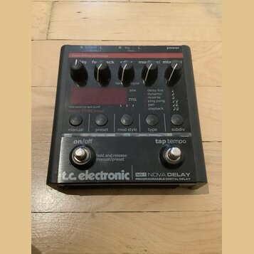 Černý efekt pedál s nápisy „Guitar Effects Technology“ a „tc electronic ND-1 NOVA DELAY PROGRAMMABLE DIGITAL DELAY“. Zařízení má šest ovládacích knof…