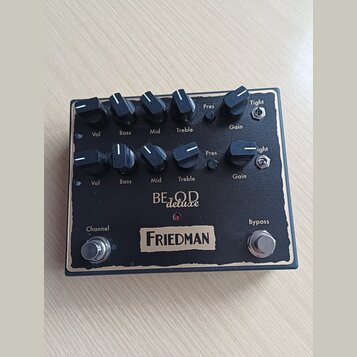 Černý kytarový efekt s nápisy BE O.D deluxe a FRIEDMAN. Na horní straně se nachází dvě řady ovládacích knoflíků s popisky Vol, Bass, Mid, Treble, Pre…
