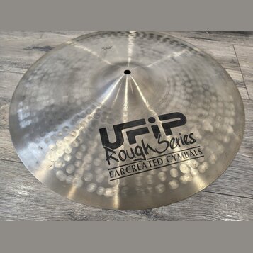 Kovový činel s kovaným povrchem a viditelnými důlky. Na povrchu je černý nápis UFIP Rough Series EARCREATED CYMBALS. V horní části je malý, nečitelný…