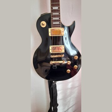 Černá elektrická kytara s gold hardwarem a hnědým hmatníkem. Na těle jsou dva humbuckery, čtyři otočné knofíky a přepínač s nápisy RHYTHM a TREBLE. P…