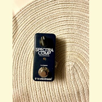 Tmavě modrý kytarový pedál s nápisem SPECTRA COMP a BASS COMPRESSOR. Ve spodní části je uveden text true bypass a logo tcelectronic. Pedál má jeden o…