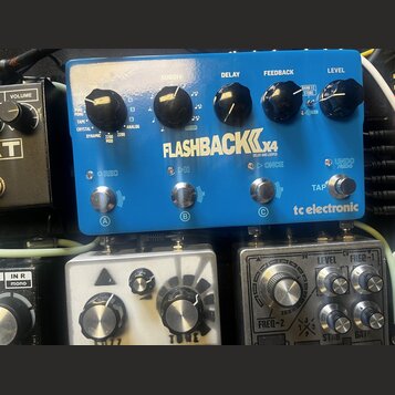 Modrý efekt pedál s nápisy FLASHBACK x4 a tc electronic. Na horní části jsou vypsány typy delay efektů, včetně názvů TAPE, ANALOG a CRYSTAL. Pedál má…