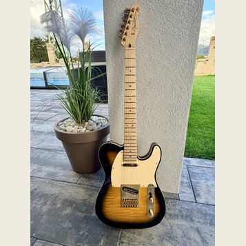 Elektrická kytara s tělem v provedení sunburst a bílým pickguardem. Na hlavě hředu je viditelné logo Fender. Kytara má světle dřevěný hmatník a zlaté…