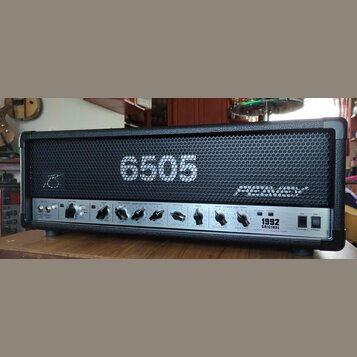 Kytarový zesilovač s černým povrchem a kovovou mřížkou. Na mřížce je bílý nápis 6505 a logo PEAVEY. Spodní ovládací panel obsahuje různé potenciometr…