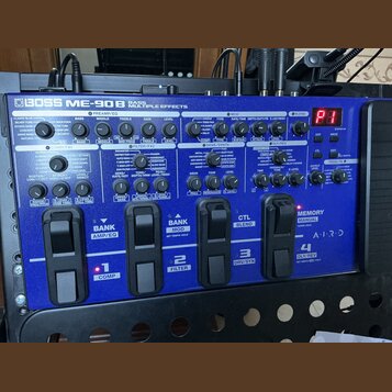 Modrý efektový procesor s nápisem BOSS ME-90B BASS MULTIPLE EFFECTS. Zařízení obsahuje numerous ovládací knofíky, přepínače a čtyři stupněbarevné ped…