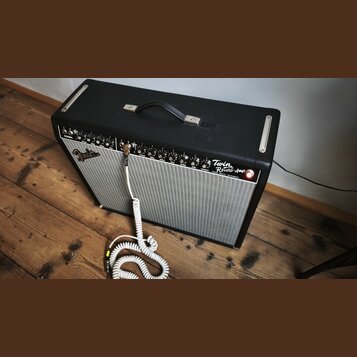 Kytarový kombozesilovač s černým texturovaným potahem a stříbrnou textilní maskou. Na předním panelu je vlevo logo Fender a vpravo nápis Twin Reverb-…