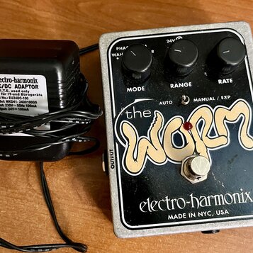 Kytarový efekt v kovovém šasi s černým povrchem a nápisem the WORM a electro-harmonix MADE IN NYC, USA. Na horní straně jsou tři černé otočné ovnovát…