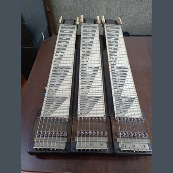 Tři stejné hmatníky pedal steel guitar z tmavého dřeva s bílými vložkami a černým rastrem. Každý hmatník má v horní části čtyři bílé ladičky a v doln…
