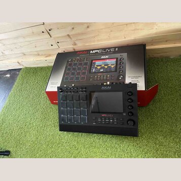 Černý sampler MPC Live II značky AKAI PROFESSIONAL. Zařazení obsahuje 16 gumových padů, displej a ovládací knofíky. Na přístroji je viditelný nápis M…