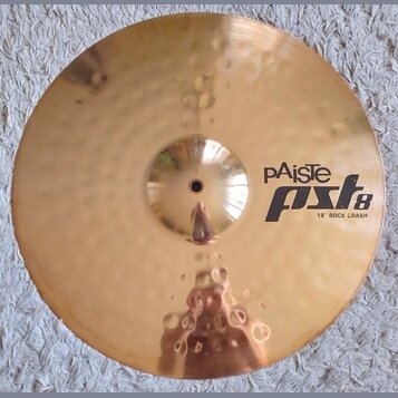 Zlatý kovový činel s povrchem s jemnými kladenými důlky. Na pravé straně je černý nápis pAiste pst8 18" ROCK CRASH. Povrch je v dobrém stavu bez vidi…