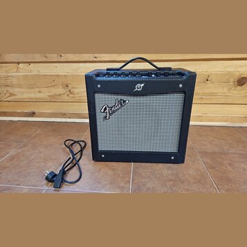 Černý kytarový kombozesilovač s šedou textilní maskou reproduktoru. Na masce je bílý nápis Fender a nad ní se nachází malé kulaté logo. Horní panel o…