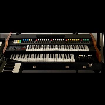 Černý dvoumanuálový synthesizér s dřevěnými bočními panely. Horní panel obsahuje řadu barevných tlačítek a posuvníků, vpravo na spodním panelu je náp…
