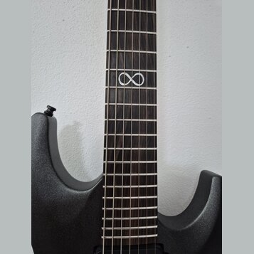 Detail elektrické kytary s tmavým hрифem a černým trupem s kovovým leskem. Na hрифu je v jedné z poloh vložena bílá značka ve tvaru symbolu nekonečna…