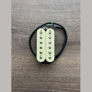 Fotografie znázorňuje humbucker snímač v krémové barvě s dvěma řadami šesti viditelných šroubů. Snímač má připojovací kabel v černém oplastu s odhale…