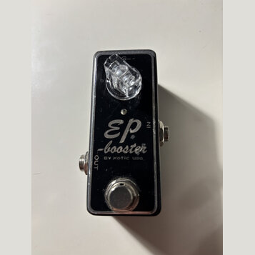 Černý kytarový efekt pedál v kovovém šasi. Na povrchu je bílý nápis „EP -booster BY xotic usa.“ a označení vstupů „IN“ a „OUT“. V horní části je průh…
