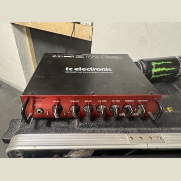 Černý basový zesilovač s červeným předním panelem. Na horní části je bílý nápis tc electronic a text DESIGNED AND ENGINEERED IN DENMARK. Na předním p…