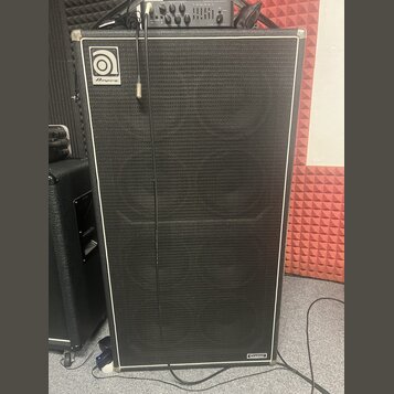 Černý basový reproduktor s bílým lemováním a kovovými rohy. V levém horním rohu je logo Ampeg a v pravém dolním rohu nápis CLASSIC. Povrch je potahen…