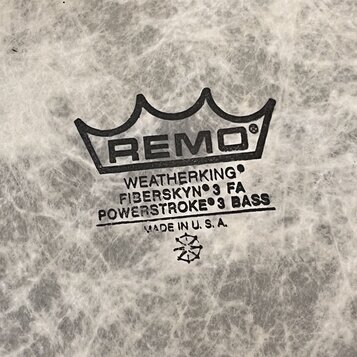 Detailní záběr na bílou bubnovou blánu s mramorovým vzorem. Uprostřed je černý nápis REMO v koruně a text WEATHERKING, FIBERSKYN 3 FA, POWERSTROKE 3…