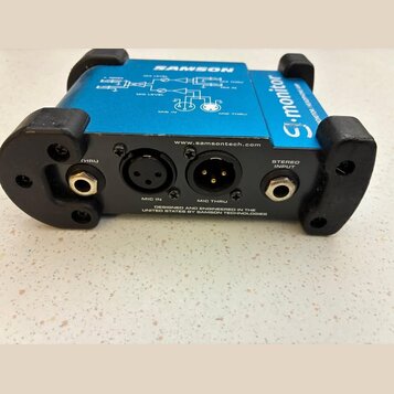 Modrý elektronický přístroj s černým plastovým rámem a nápisy SAMSON a S-monitor. Na zadní straně jsou konektory s popisky THRU, MIC IN, MIC THRU a S…